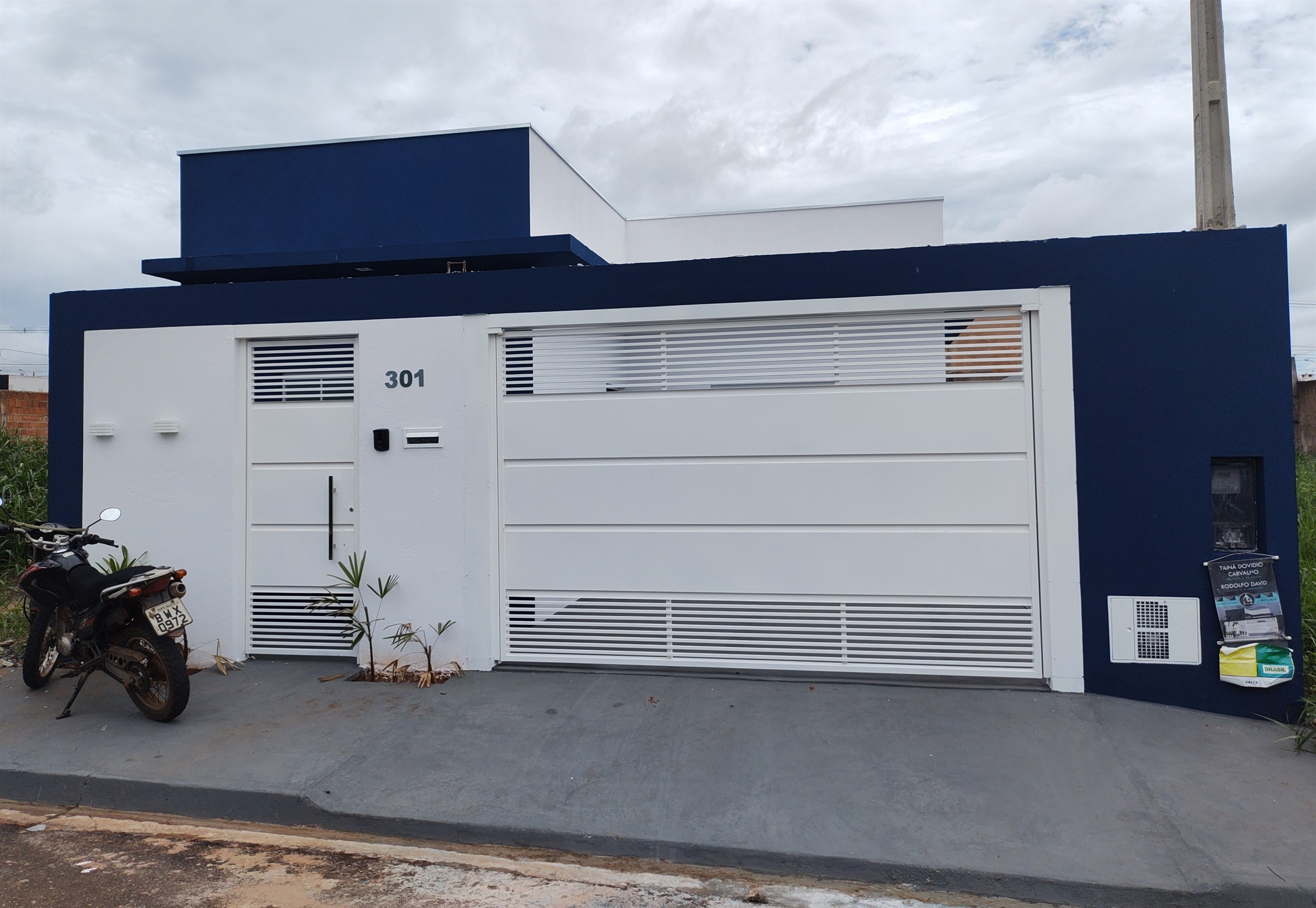 Fachada entregue em azul e branco, com portão de garagem e porta social em alumínio branco