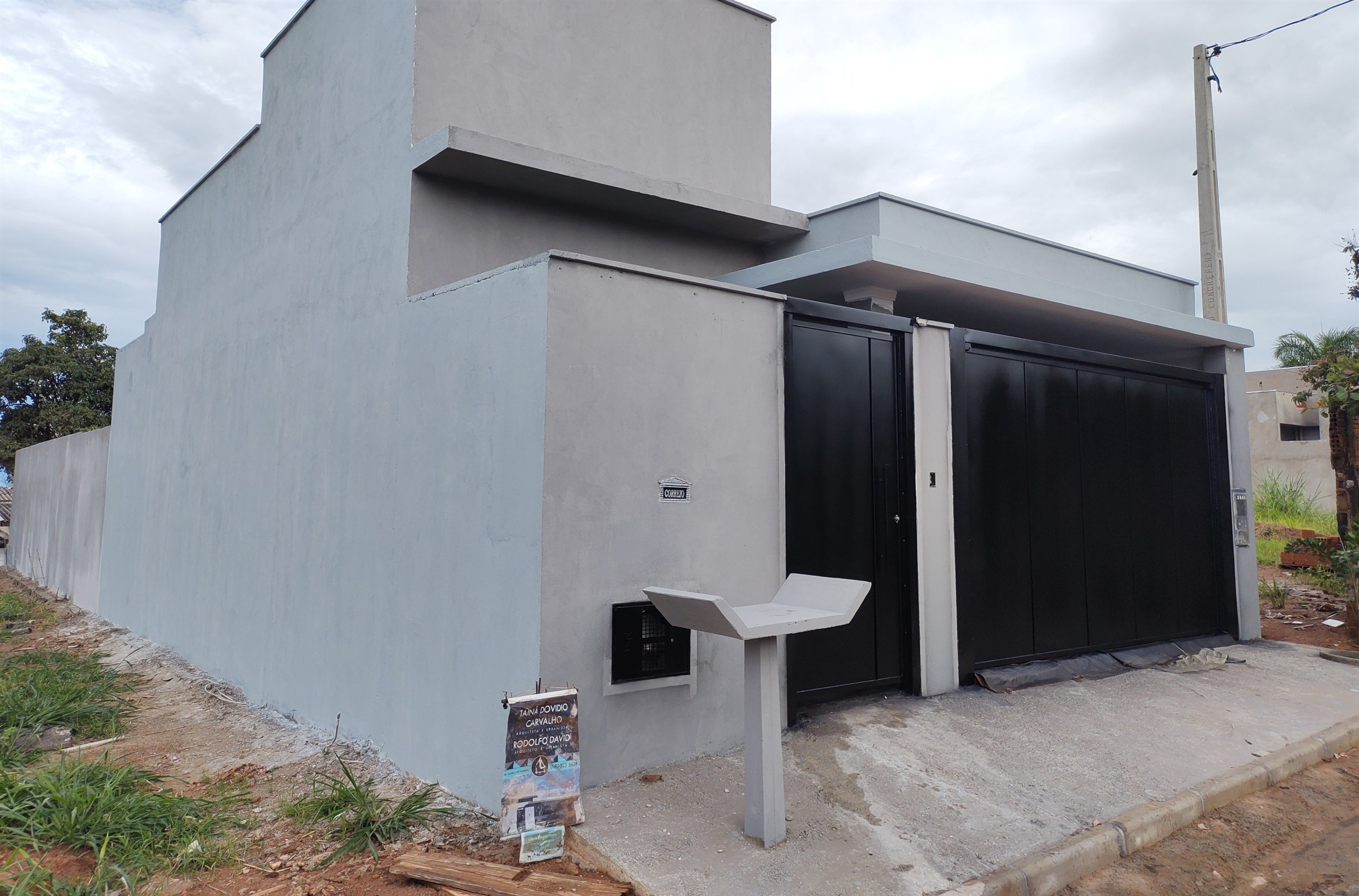 Fachada entregue em tons de cinza, com recuo lateral, portão escuro e caixa de correio