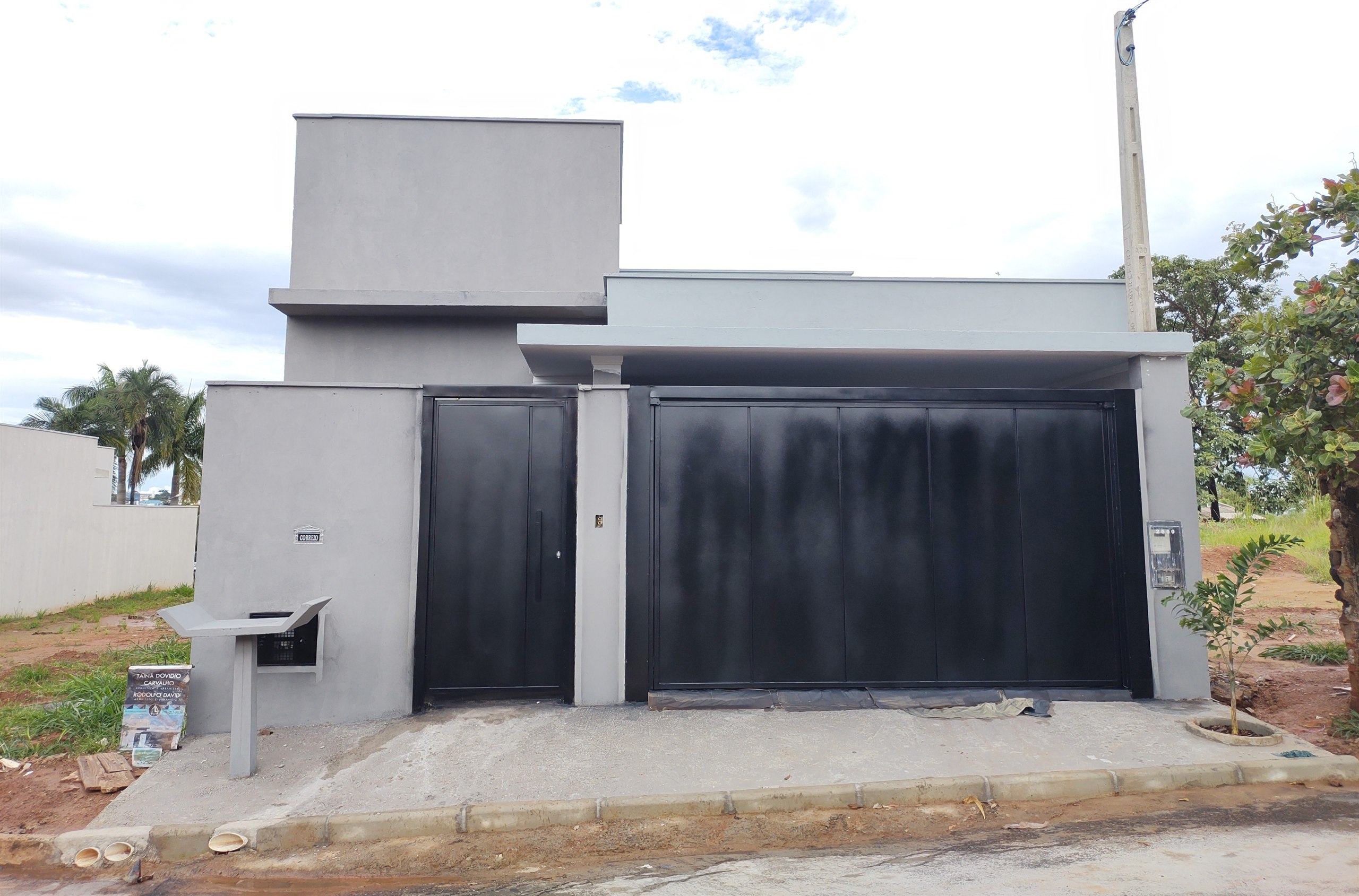 Fachada entregue com volumes retos em cinza, portão de correr escuro e calçada concluída