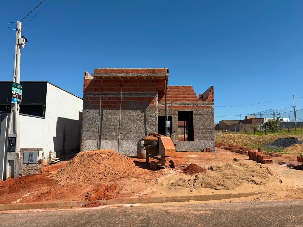 Estrutura de casa em construção com alvenaria de tijolo aparente e betoneira no canteiro