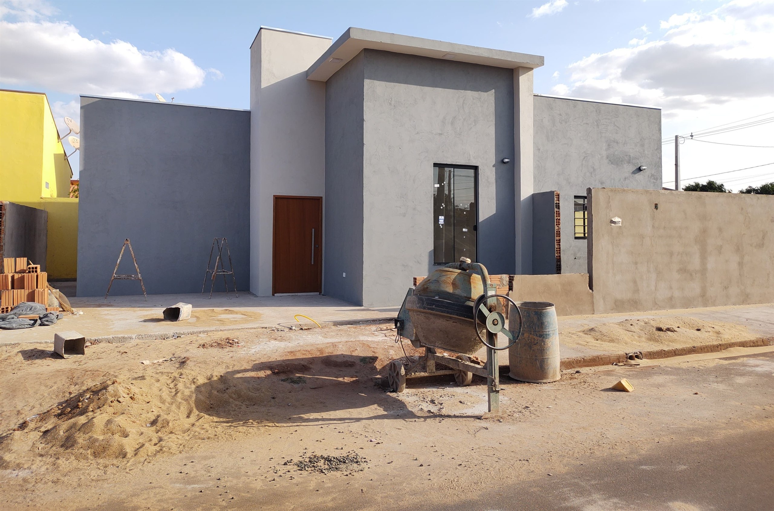Casa em fase de acabamento externo, com fachada já rebocada e materiais no canteiro